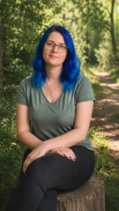 Photo d'Alice, psychologue, se trouvant en forêt, assise sur un tronc d'arbre. Grâce à l'IA, la couleur de ses cheveux a été modifiée pour être bleu, comme elle en rêve secrètement.